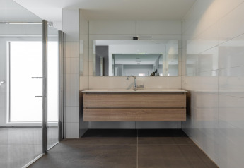 Baño moderno con tocador flotante de madera, gran espejo y ducha de cristal en Holiday Park Latour 6, Países Bajos.