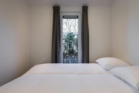 Camera con letto matrimoniale, pareti bianche, finestra con tende e vista giardino presso Holiday Park Latour 8, Paesi Bassi.