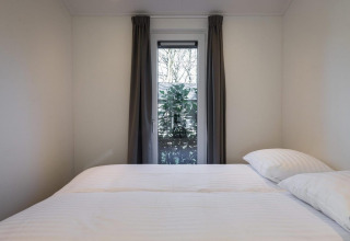Dormitorio con cama doble, paredes blancas, ventana con cortinas y vista al jardín en Holiday Park Latour 8, Países Bajos.