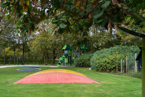 Outdoor playground at a lodge featuring a colorful air pillow, swings, and a slide, surrounded by trees.