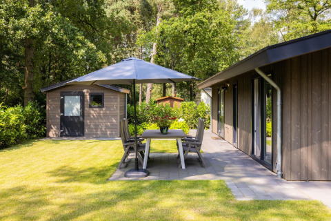 Udendørs område ved Holiday Park Latour 8 i Holland med terrasse, borde, stole og parasol i haven.