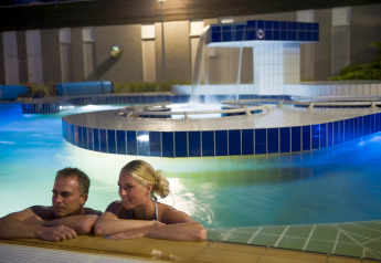 Una pareja se relaja de noche en una piscina iluminada en un glamping con instalaciones modernas.