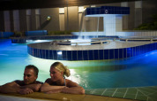 Una pareja se relaja de noche en una piscina iluminada en un glamping con instalaciones modernas.