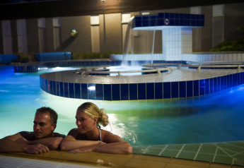 Ein Paar entspannt sich abends in einem beleuchteten Pool bei einer luxuriösen Glamping-Unterkunft.
