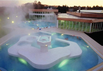 Buiten spa- en zwembad bij schemering op een glamping accommodatie met stoom en moderne glasarchitectuur.