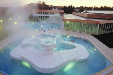 Espace spa et piscine extérieure au crépuscule dans un site de glamping, avec vapeur et architecture moderne.