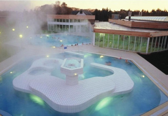 Udendørs spa- og poolområde ved skumring i et glampingophold med damp, modernistisk design og glasfacader.