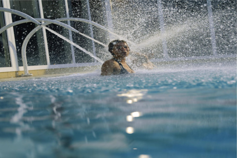 Persona disfrutando de los chorros de agua en una piscina cubierta dentro de un alojamiento glamping.