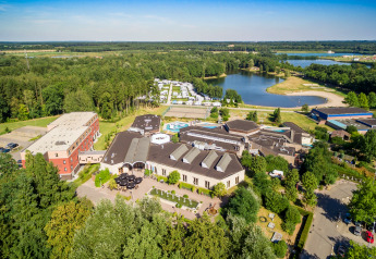 Aerial view of a glamping accommodation with cabins, a lake, and lush green surroundings near a forest.