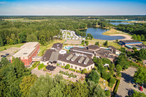 Vista aérea de un alojamiento glamping con cabañas, lago y vegetación en un entorno natural y tranquilo.