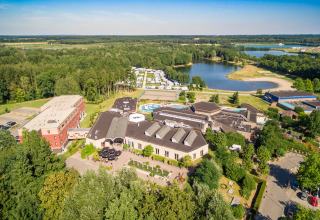 Aerial view of a glamping accommodation with cabins, a lake, and lush green surroundings near a forest.
