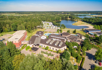 Aerial view of a glamping accommodation with cabins, a lake, and lush green surroundings near a forest.