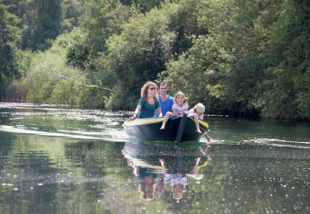 Family enjoying a peaceful boat ride on a lake surrounded by lush greenery near a glamping site.