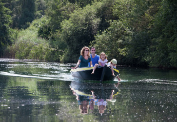 Family enjoying a peaceful boat ride on a lake surrounded by lush greenery near a glamping site.