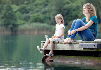 Madre e hija se relajan en un muelle de madera junto al lago, disfrutando del glamping en la naturaleza.