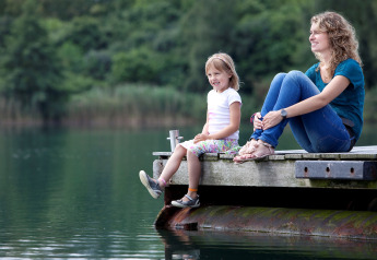 Mother and daughter relaxing on a wooden dock by the lake, enjoying a tranquil glamping experience.