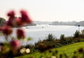 Vue sur une rivière paisible depuis un hébergement glamping, avec pelouse et fleurs floues au premier plan.