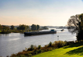 View from a glamping accommodation overlooking a river, with passing cargo boats and lush greenery.