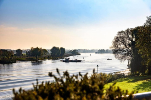 Vista di un fiume tranquillo con alberi e una barca, fotografata da un alloggio glamping al sole.