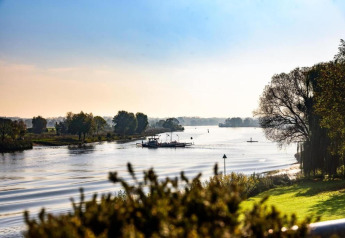 View of a serene river, trees, and a ferry boat, captured from a glamping accommodation on a sunny day.