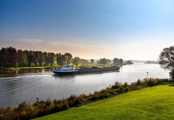 View from a glamping site showing a river barge, lush greenery, and trees under a clear blue sky.