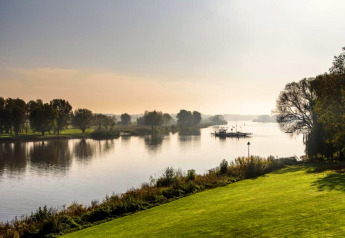 Vue paisible sur la rivière avec pelouses vertes, arbres et un ferry prise depuis un hébergement glamping.