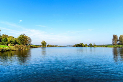 Vista de un tranquilo río con árboles verdes y cielo azul desde un alojamiento glamping en plena naturaleza.