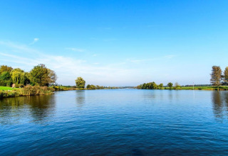 Vista su un tranquillo fiume con alberi verdi e cielo azzurro presso un alloggio glamping nella natura.
