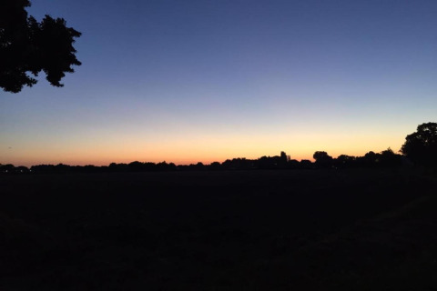 Ciel au coucher du soleil dans un hébergement glamping, silhouettes d'arbres dans une nature paisible.