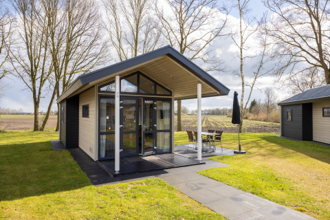 Tiny house moderna Holiday park Tolplas 19 con facciata in vetro, terrazza e giardino in una giornata di sole.