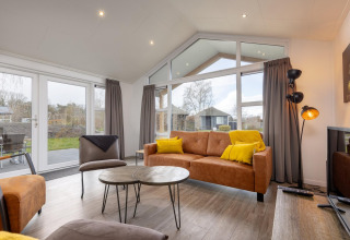 Moderne stue i en lodge i Holiday park Tolplas 18 i Holland med store vinduer og komfortable møbler.
