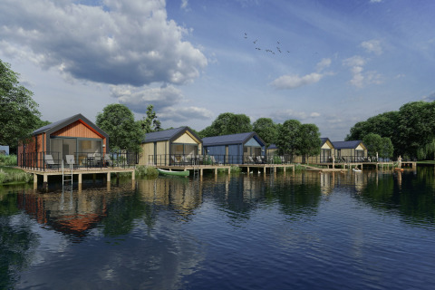 Feriehytter på pæle ved søen i Holiday Park Klein Vink 24, omgivet af træer og en rolig himmel.