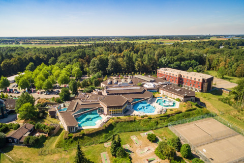 Vista aérea de un alojamiento glamping con piscinas, áreas deportivas, edificios principales y naturaleza alrededor.