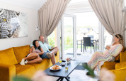 Three people relaxing on yellow sofas in a bright living room at Berg Lodge in the Netherlands, doors open.