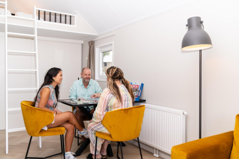 Tre personer hygger sig med et brætspil i en moderne, lys stue på Berg Lodge i Holland.