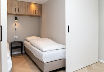 Modern bedroom at Berg Lodge in the Netherlands with a single bed, bedside table, and wall lamp.