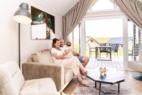 Familie nyder tid sammen i en lys stue på Berg Lodge i Holland med udsigt til terrasse og hytter.