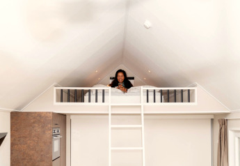 Woman relaxing on a loft bed at Berg Lodge in the Netherlands, beneath a bright and spacious ceiling.