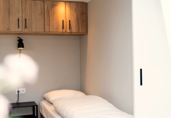 Modern minimalist single room at Berg Lodge in the Netherlands featuring wooden cabinets and a single bed.