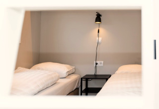 Twee eenpersoonsbedden met wit beddengoed en een zwart nachtkastje in Berg Lodge, Nederland, gezien door een raam.