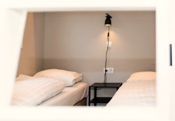 Deux lits simples avec draps blancs et table de nuit noire à Berg Lodge aux Pays-Bas, vus à travers une fenêtre.