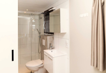 Salle de bain moderne à Berg Lodge aux Pays-Bas avec douche, toilettes, lavabo blanc et miroir.