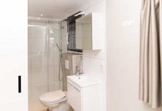 Moderne badeværelse på Berg Lodge i Holland med brusekabine, toilet og hvid vask med spejl.