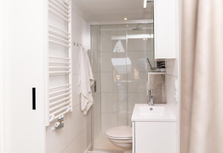 Moderne, lyst badeværelse på Berg Lodge i Holland med brusekabine, håndklæde og hvidt interiør.