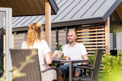 To personer nyder en afslappet morgenmad udendørs ved Berg Lodge i Holland, omgivet af grønt.