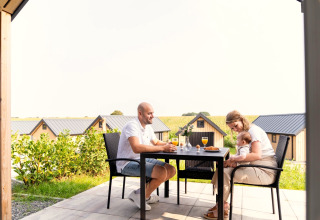Gezin ontbijt samen buiten op het terras van Berg Lodge in Nederland, met huisjes op de achtergrond.