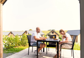 Famille prenant le petit déjeuner en terrasse au Berg Lodge aux Pays-Bas, des chalets visibles en arrière-plan.