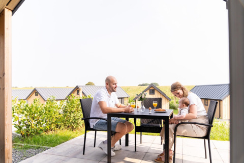 Familie nyder morgenmad sammen udenfor på terrassen ved Berg Lodge i Holland med små hytter i baggrunden.
