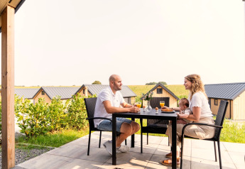 Famille prenant le petit-déjeuner sur la terrasse de Berg Lodge aux Pays-Bas avec des chalets à l’arrière-plan.