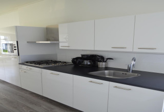 Cucina moderna del lodge “Biebosch” Sunshower nei Paesi Bassi con mobili bianchi e piano nero.